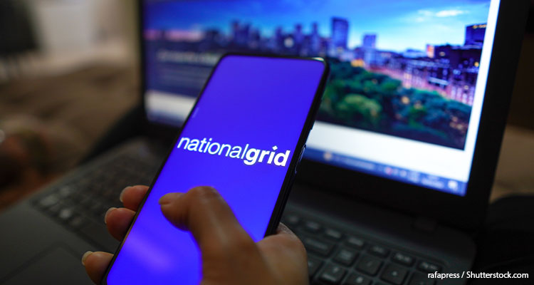 A phone with the words "national grid" is being held up in front of a laptop.