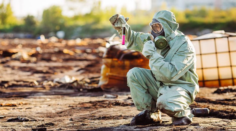 Man with gas mask and green military clothes exploring barrels and mud for nuclear waste