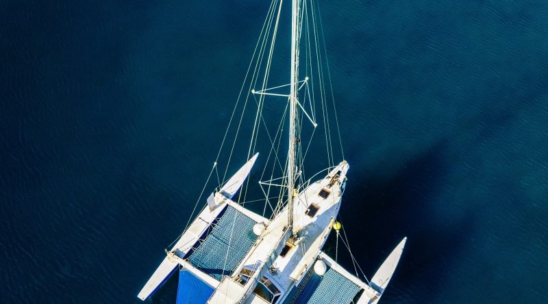 A luxurious sailing ship with masts, incorporating advanced hybrid propulsion technology, set against a blue ocean backdrop. The ship showcases a blend of traditional sailing design and modern environmental technology, including solar panels.