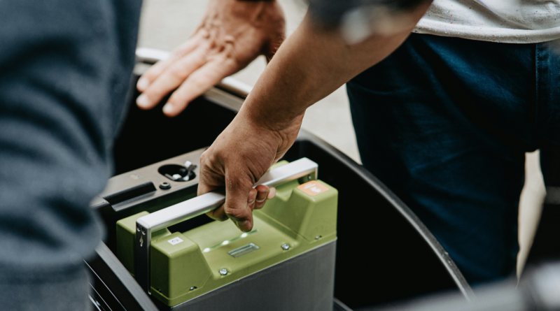 A person lifting a portable lithium-ion battery, representing modern energy storage solutions for homes and electric vehicles.