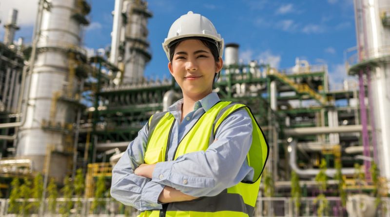 A woman in safety gear standing in front of an oil and gas plant, representing women in the oil and gas industry.