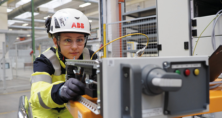 a worker servicing ABB industrial electrical equipment while wearing a hard hat and safety glasses