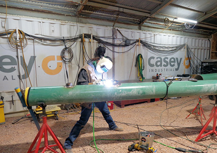 a welder performing pipeline welding on a large green pipe section