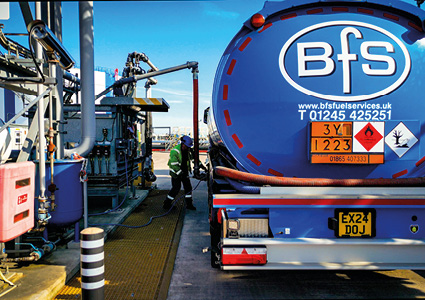a commercial fuel tanker truck parked at an industrial fuel loading depot, positioned next to automated delivery equipment