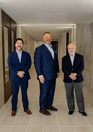 a group of three individuals dressed in professional business attire, standing together in a brightly lit hallway