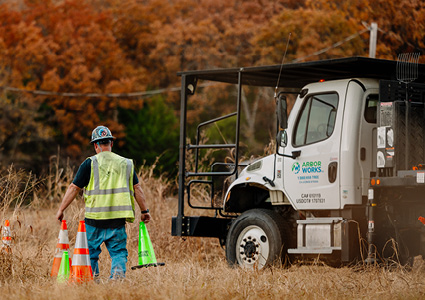 a utility or arborist truck from Green Works parked in a field, with a worker setting up safety cones