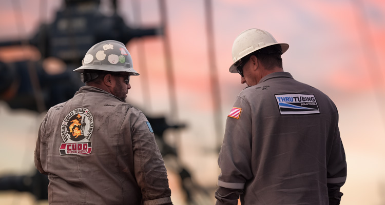 two oilfield workers standing in front of oil drilling equipment at dusk