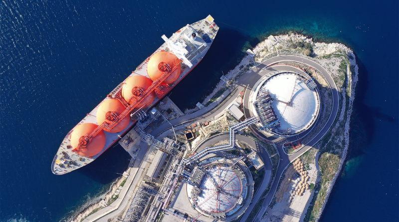 Aerial view of an LNG carrier loading at a liquefied natural gas export terminal with two large storage tanks.