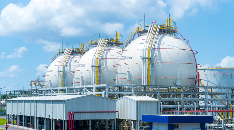 A row of large industrial spherical storage tanks at a petrochemical plant under a bright blue sky with clouds.
