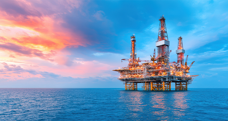 This image captures a stunning view of an offshore oil rig platform against a backdrop of a vibrant sunset The platform stands tall in the middle of the vast blue ocean while the sky above displays a range of hues from pink to orange reflecting