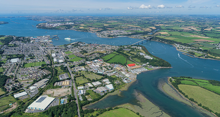 a wide, sweeping view of a coastal waterway winding through a mix of urban development and green countryside