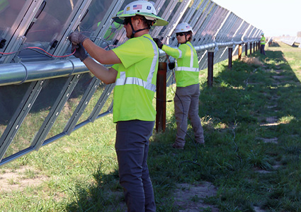 utility workers installing electrical wiring and components on a ground-mounted solar tracker array at a utility-scale solar farm
