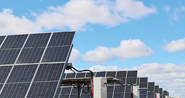 a utility-scale solar photovoltaic (PV) farm featuring rows of ground-mounted solar panels under a partly cloudy blue sky